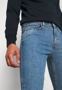 Ljusblå denimjeans med en figurnära design, femficksstil och subtila blekningar. I kombination med en svart långärmad tröja.