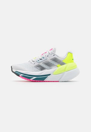 Witte atletieksneaker met zilveren strepen, neongele hiel, accenten in groenblauw en roze op de zool, en een bovenwerk van mesh voor ademend vermogen.