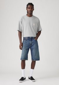 Gray cotton t-shirt with short sleeves and a chest pocket, paired with denim shorts, white crew socks, and black slip-on shoes.