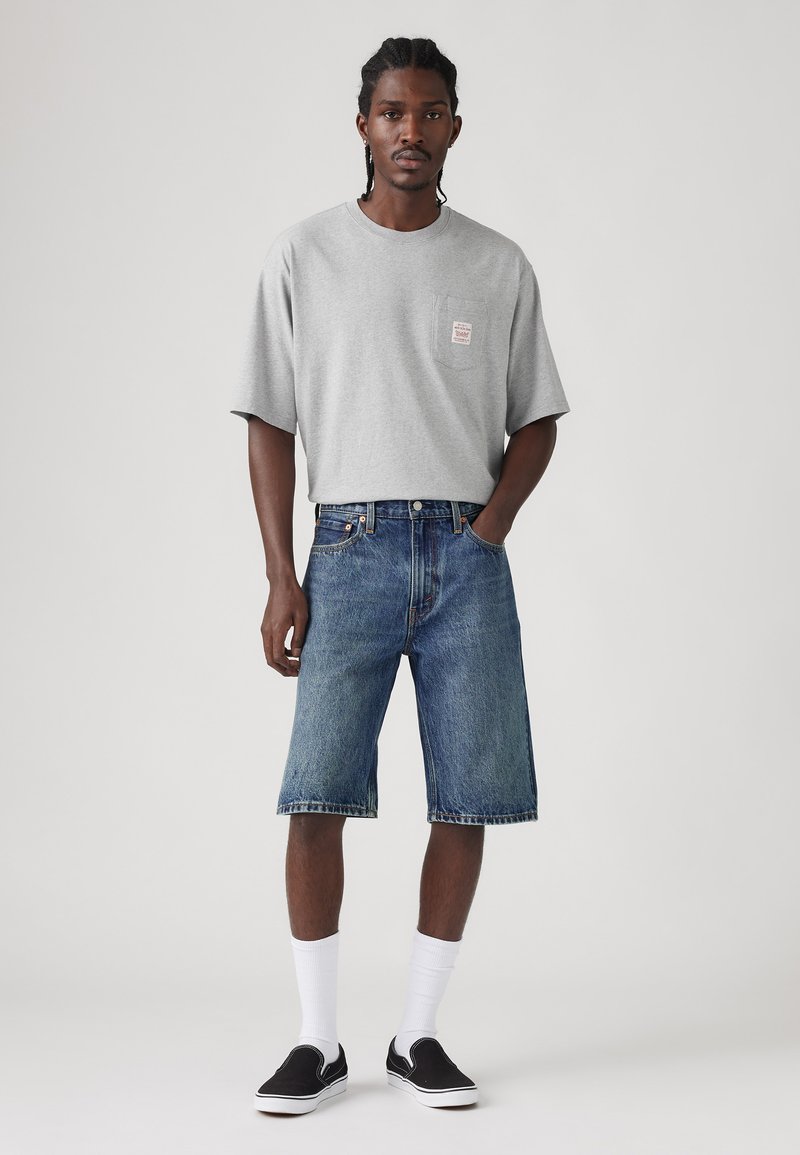 Gray cotton t-shirt with short sleeves and a chest pocket, paired with denim shorts, white crew socks, and black slip-on shoes.