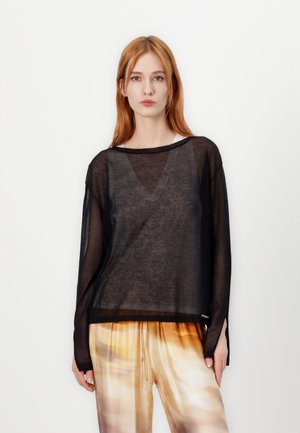 Zwarte, semi-doorzichtige, lange mouwen top met een V-halslijn, voorzien van een losse pasvorm en verlaagde schouders, gedragen over gemusterde, lichte broek.