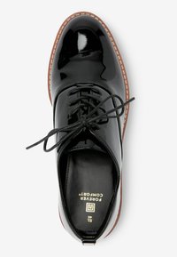 Chaussure à lacets en cuir verni noir avec un bout rond, semelle plate et des détails cousus en marron. Présente des lacets noirs et une semelle intérieure texturée.