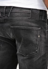 Vaqueros de mezclilla negra con una textura desvaída. Presenta dos bolsillos traseros, costura curva en el bolsillo izquierdo y una etiqueta de marca de cuero.