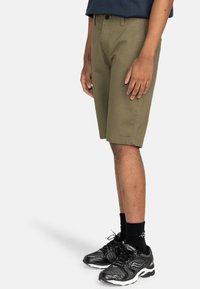 Olivgröna shorts i bomull, med knäppning och sidofickor. Kombination med svarta träningsskor och strumpor.