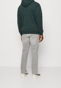 Haut à capuche vert foncé, jeans gris et baskets blanches. Le haut à capuche présente une poche kangourou et des poignets côtelés ; les jeans sont ajustés avec une texture délavée.