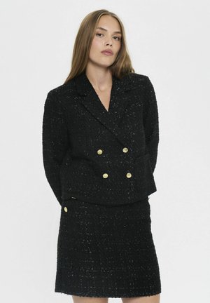 Schwarzer, strukturierter Tweed-Blazer mit doppelter Knopfleiste und goldenen Knöpfen, kombiniert mit einem passenden Rock. Glatte und taillierte Silhouette.