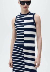 Top senza maniche a righe blu navy e bianche con texture a coste, caratterizzato da un design a blocchi di colore. Abbinato a una gonna a righe coordinata.