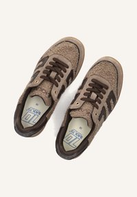 Bruine sneakers met een gestructureerd zeemleren bovenwerk, donkerbruine suede accenten, gouden veterogen en een vetersluiting. Van binnen heeft het een maatlabel.