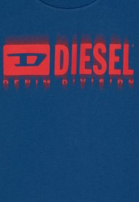 Tessuto blu con logo rosso Diesel Denim Division e lettering stilizzato che sfuma verticalmente verso il basso.