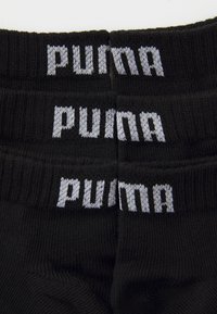 Calcetines negros con textura acanalada, que presentan el logotipo gris de "puma" tejido en el puño. Tres pares apilados, mostrando la alineación del logotipo.