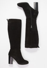 Bottes noires en daim montantes avec un talon épais, dotées d'une fermeture éclair sur le côté et d'un design de pointe lisse. La texture douce améliore l'attrait visuel.