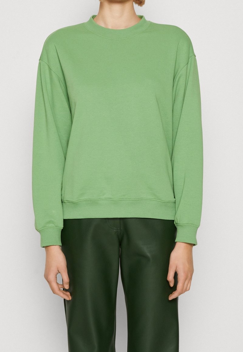 Sudadera de manga larga en algodón verde claro con cuello redondo, corte relajado, puños y dobladillo acanalados; combinada con pantalones verdes oscuros.