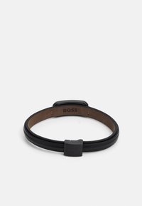 Black leather bracelet with a smooth finish, featuring a metallic black clasp and a soft brown interior with embossed logo.