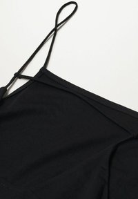 Černá tílko s tenkými ramínky, které má hladkou texturu a jednoduchý design. Ramínka mají nastavitelné smyčky pro přizpůsobení velikosti.