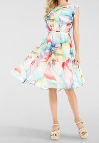 Blommig klänning i pastellfärger med korta ärmar, figurnära midja och utsvängd kjol. Bärs med beige kilklackar.