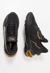Schwarze Sportschuhe mit goldenen Akzenten, Obermaterial ausMesh, strukturierte Gummisohle und ausgeprägte Profilstollen an der Ferse. Puma-Logo auf der Zunge.
