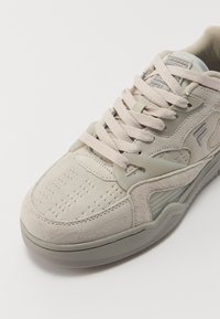 Beige Wildlederschuhe mit hellrosa Schnürsenkeln, strukturiertem Gummisole und Markenlogo an der Seite und Zunge.