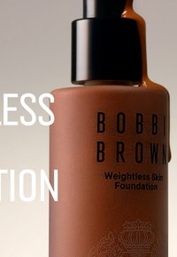 Bobbi Brown Weightless Skin Foundation i en mat brun flaske, med en svart pumpe og preget detaljering på bunnen. Lquid foundation drypper.