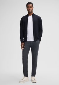 Schwarze Zip-Jacke, weißes T-Shirt, graue strukturierte Hose und helle Sneaker. Verfügt über eine lockere Passform und elegante Linien.