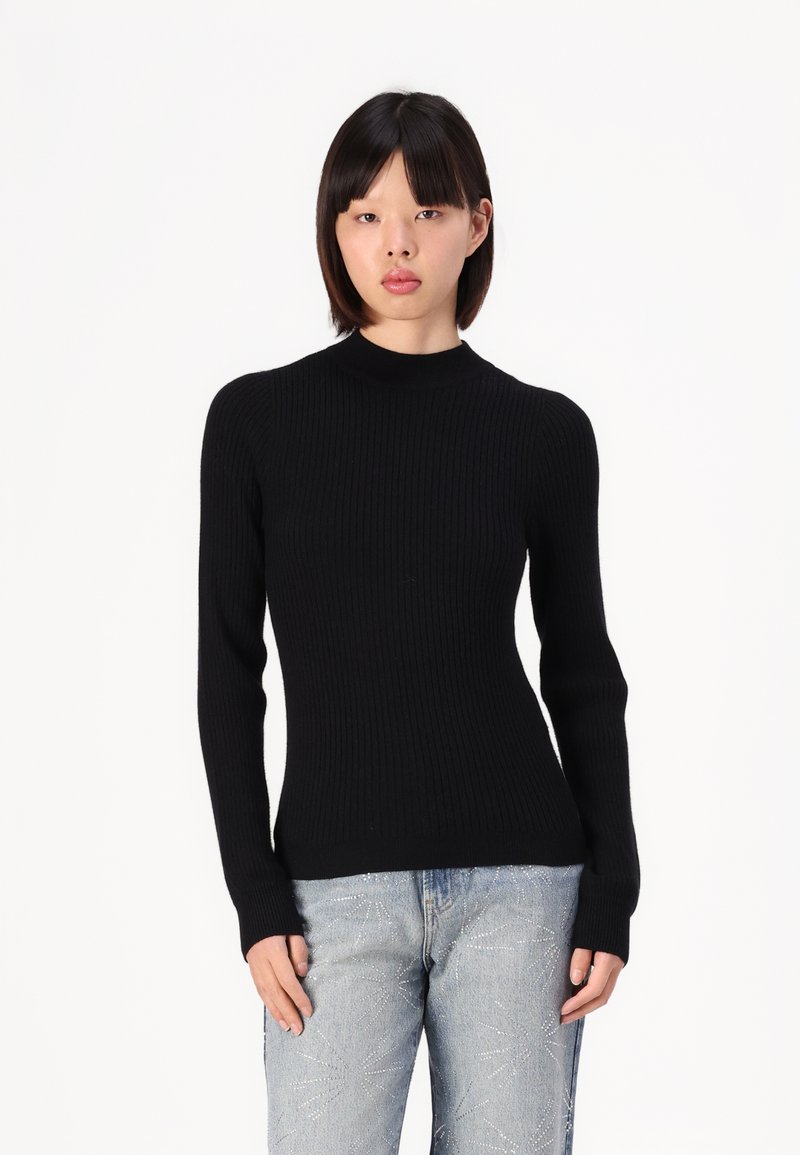 Pull en tricot noir côtelé avec un col montant et des manches longues, associé à un jean délavé clair avec des embellissements subtils.