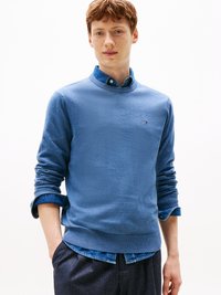 Modra pletena pulover s okroglim izrezom in zavihanimi rokavi, prekrit s jeans srajco. Ima majhen logotip na levem prsnem delu.