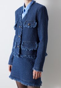 Costume en tweed bleu avec des bords effilochés, deux poches avant avec des accents de boutons, et un design ajusté avec une jupe courte assortie.