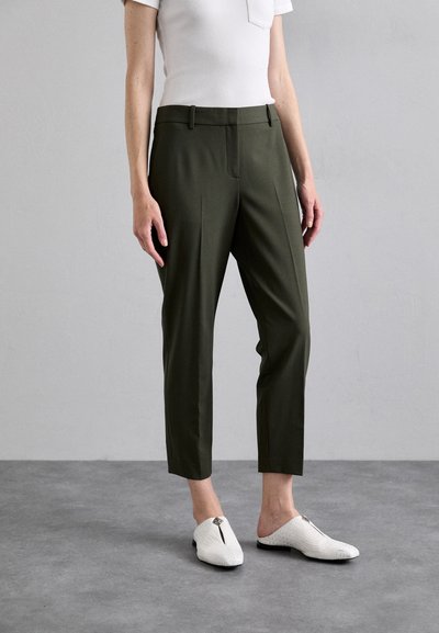 Pantalons taillés en vert olive avec un devant plat, des poches latérales et une longueur légèrement cropped. Associés à des chaussures blanches à enfiler texturées.