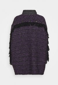Cape en laine texturée violette et noire avec franges noires et boutons-pression noirs le long du haut du dos, présentée sur fond blanc.