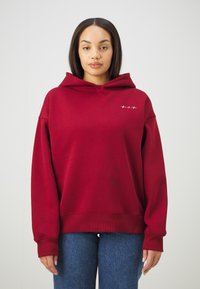 Bordeauxrote Kapuzenjacke mit einer Kängurutasche, gerippten Bündchen und Saum. Verfügt über ein kleines weißes Logo auf der Brust. Weicher Stoff mit einer lockeren Passform.