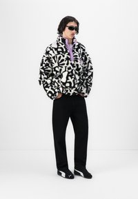 Zwart-wit gestreepte fleece trui met een paarse kraag, gecombineerd met zwarte broeken en zwarte sneakers, met een modern ontwerp.