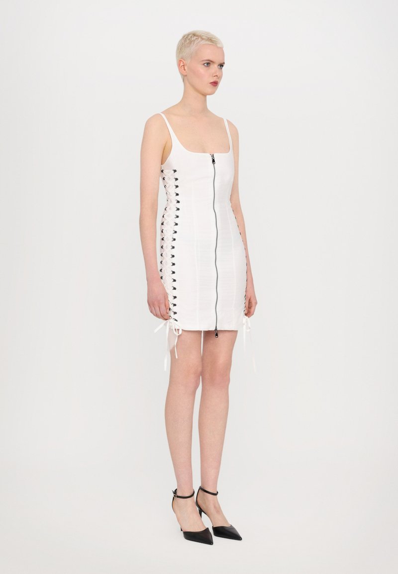 Witte mini-jurk met een vierkante halslijn, een rits aan de voorkant en zwarte vetersluiting aan de zijkanten. Glad materiaal, slim fit, verstelbare banden.