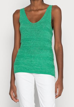 Vihreä neulottu toppi, jossa V-kaula-aukko, ribbineulos ja istuva malli. Päällä valkoiset housut.