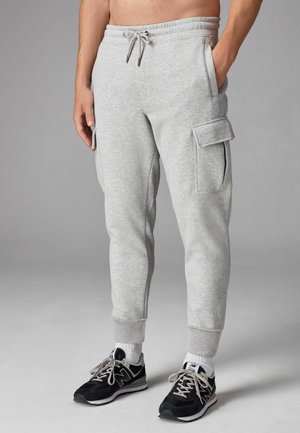 Lysegrå sweatpants med en tætsiddende pasform, elastisk talje, snøre, sidelommer og cargolommer. Båret med sorte sneakers.