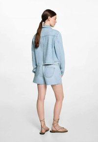 Ljusblå denimjacka och shorts-set, som har en cropped design, fransade kanter och standard bakfickor. Bruna remsandaler.