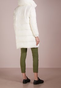 Vit puffjacka med hög krage och långa ärmar, i kombination med olivgröna slim-fit byxor och svarta sneakers. Slät textur, minimalistisk design.