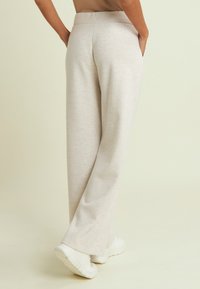 Pantaloni larghi color beige chiaro con una texture liscia, dotati di tasche laterali e vita elasticizzata. Abbinati a scarpe da ginnastica bianche.
