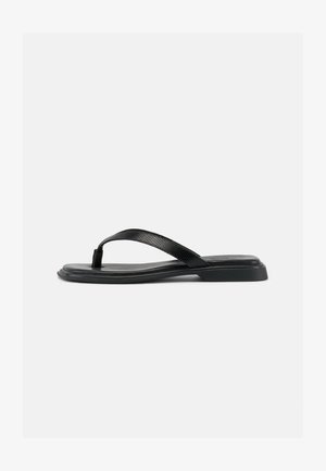 Sandale noire plate en forme de tongs avec une bride texturée et un talon légèrement surélevé, montrée en profil latéral sur un fond clair uni.