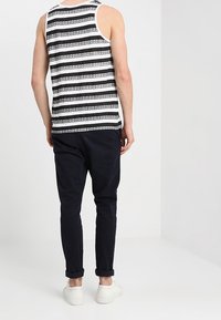 Schwarz-weiß gestreiftes Tanktop aus Baumwolle, figurbetontes Design. Kombiniert mit marineblauen Slim-Jeans mit hochgekrempelten Bündchen und weißen Sneakers.