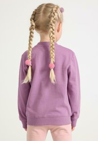 Lilla sweatshirt med rund halsudskæring, lange ærmer og ribbede manchetter. Lyserøde hårbånd fremhæver to fletninger i hestehaler.