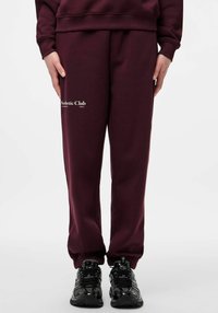 Bordo trenirke iz mehke tkanine z elastičnim pasom in manšetami. Spredaj je modno nameščen bel logotip.