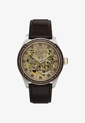 Analógové hodinky Timex s erbom Rokfortu, priehľadnými zlatými ozubenými kolesami, hnedým koženým remienkom a nápisom „Hogwarts School of Witchcraft and Wizardry“.