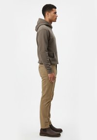Sudadera gris con un bolsillo frontal, combinada con pantalones beige y botas de tobillo marrones. Modelo mostrado de perfil contra un fondo neutro.