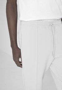 Pantalon de jogging gris clair avec une taille élastique et un cordon de serrage. Tissu doux, doté de poches latérales et de coutures surpiquées.