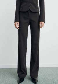 Pantaloni neri su misura con una vestibilità a gamba larga, texture liscia e vita alta. Indossati con tacchi neri a punta e una giacca aderente.