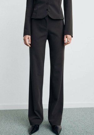 Pantaloni neri su misura con una vestibilità a gamba larga, texture liscia e vita alta. Indossati con tacchi neri a punta e una giacca aderente.