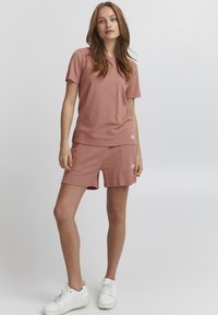 Set di t-shirt e pantaloni corti in maglia waffle color rosa, con una vestibilità rilassata, maniche corte e tasche laterali. Abbinato a sneakers bianche.