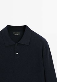 Dunkelblaues Poloshirt aus weichem Stoff, mit klassischem Kragen, zwei Knöpfen und dezentem Muster. Markenetikett am Kragen sichtbar.