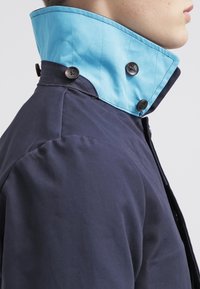 Giacca della marina con colletto azzurro chiaro, caratterizzata da cuciture strutturate e due bottoni scuri sul colletto per la chiusura.
