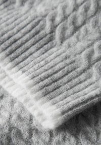 Pelēks adīts audums ar ribotu rakstu un gaišāku pelēku maliņu. Mīksta tekstūra ar redzamām šķiedrām, kārtots uz līdzīgas tekstūras fona.