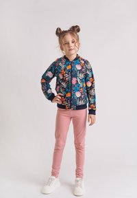 Bomberka w granatowy wzór kwiatowy z zamkiem, ściągaczami na rękawach i granatowymi wykończeniami, zestawiona z dopasowanymi różowymi spodniami i białymi sneakersami.